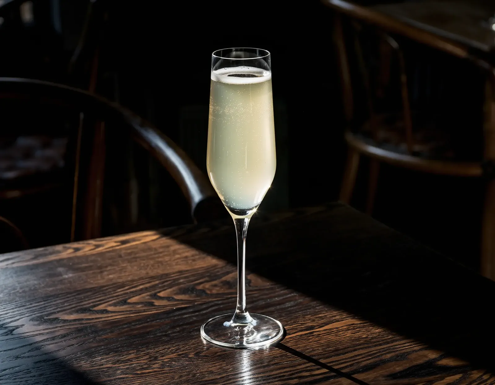Death in the afternoon cocktail in a champagne flute on a wooden table at a bar.