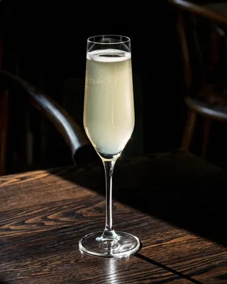 Death in the afternoon cocktail in a champagne flute on a wooden table at a bar.
